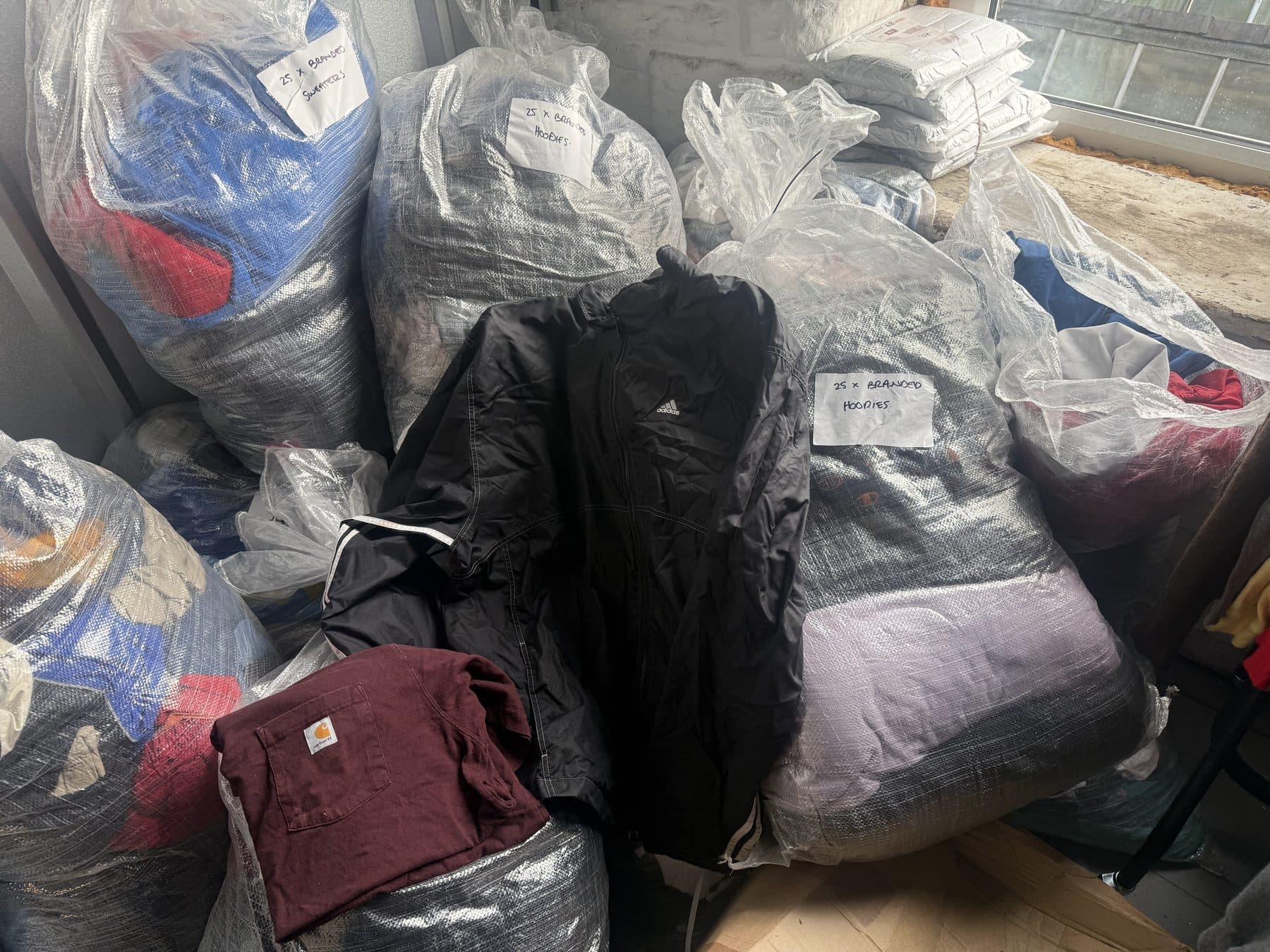 Counted lots bagged and labelled in the Burnley unit, one marked twenty-five branded hoodies, with a burgundy Carhartt t-shirt and a black adidas jacket on top.